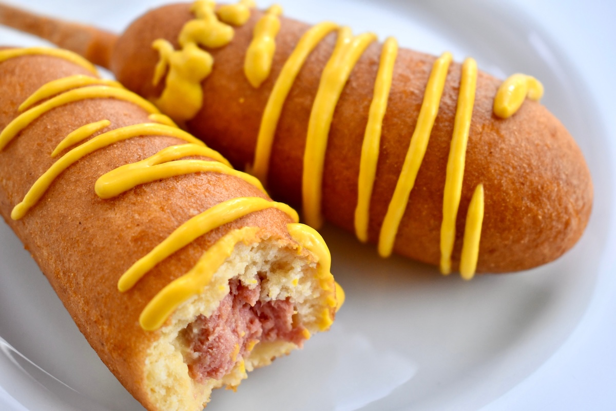 Two,Corn,Dogs,With,Mustard,On,A,White,Plate